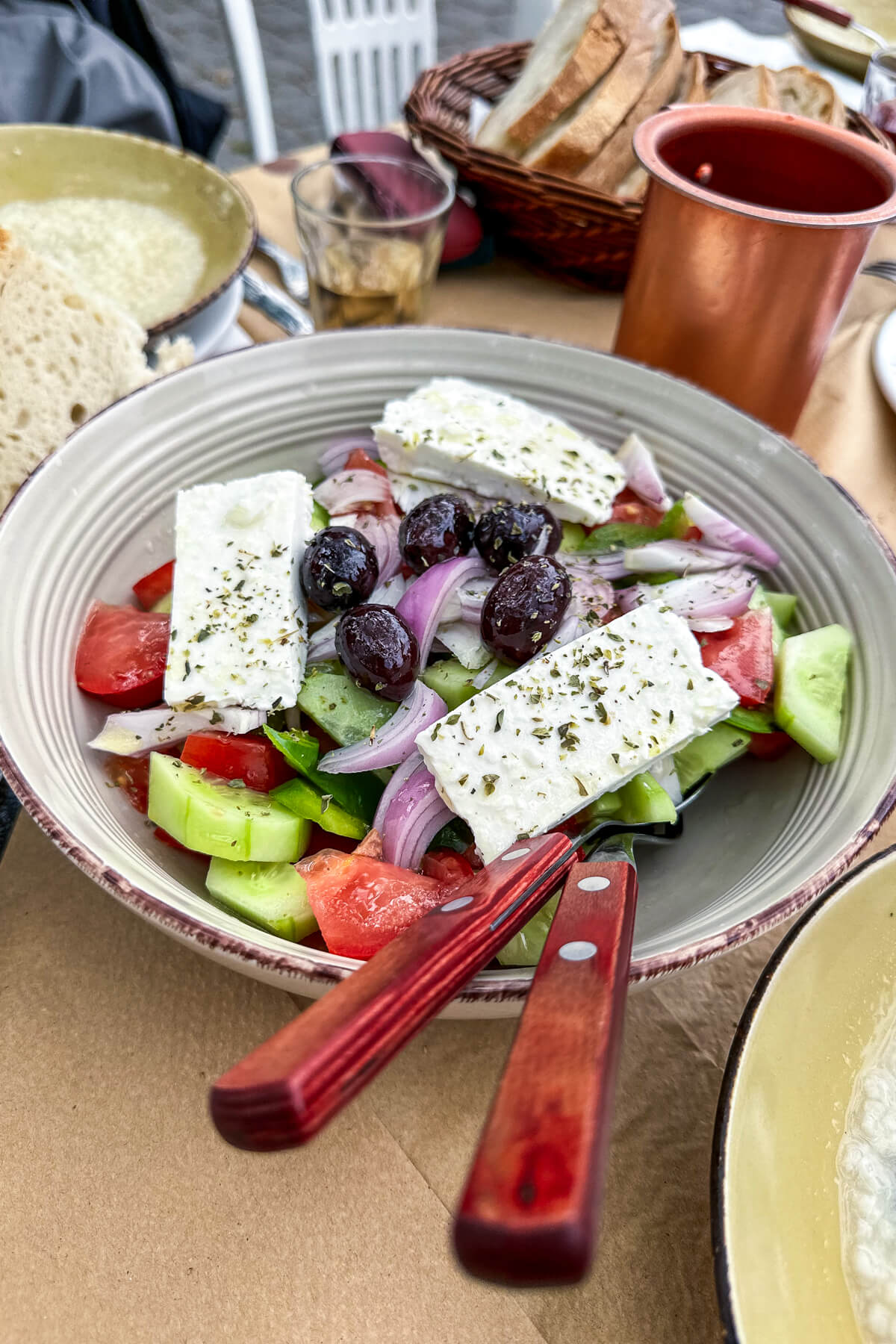 A traditional Greek cucumber salad in a white bowl with serving spoons 