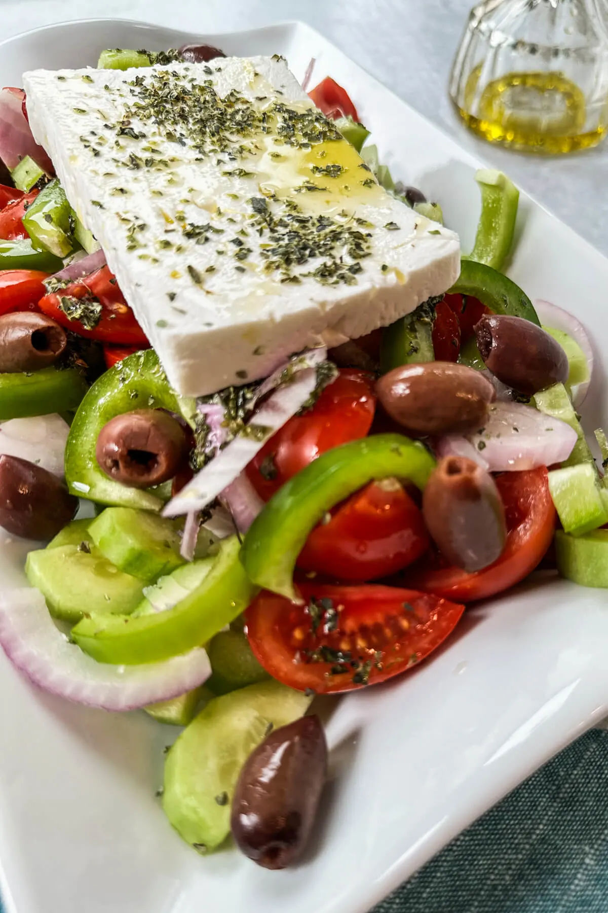Traditional Greek cucumber salad on a white serving dish with tomatoes, onions, olives, etc. and topped with a slice of feta cheese.