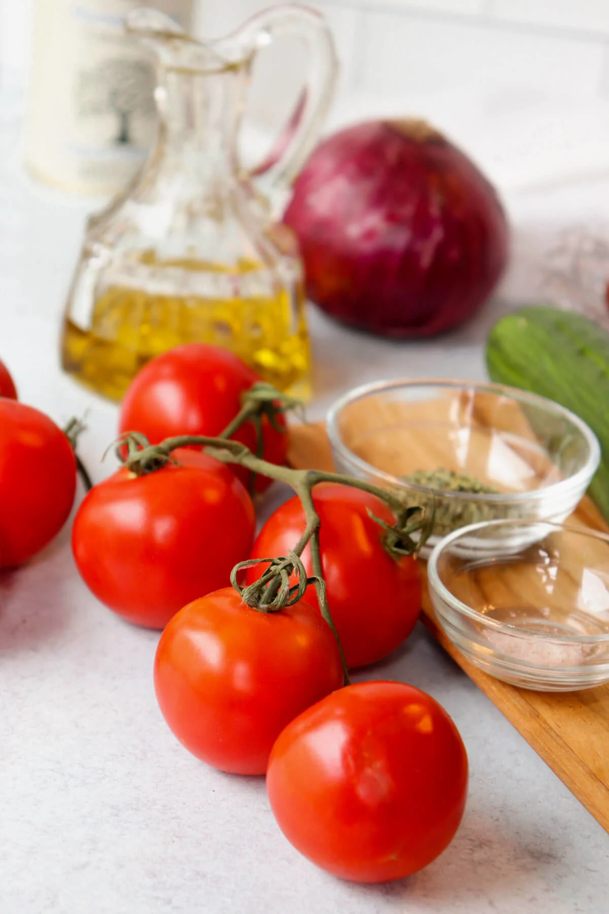 Red tomatoes on the vine with a jar of olive oil, red onion, oregano and salt