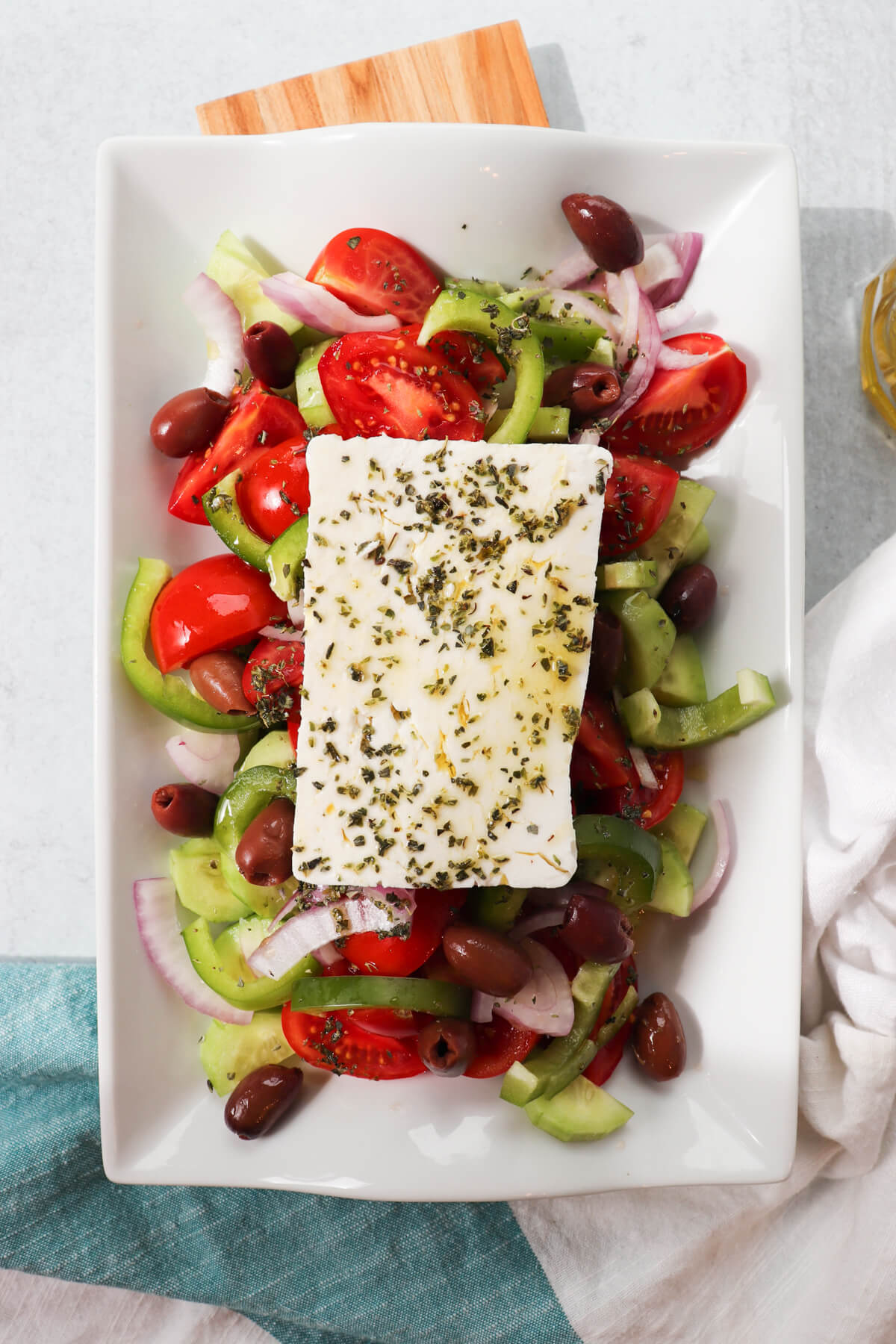 Overhead view of traditional Greek cucumber salad on a white serving dish with tomatoes, onions, olives, etc. and topped with a slice of feta cheese.