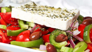 Greek cucumber salad with a piece of feta cheese on top on a white plate