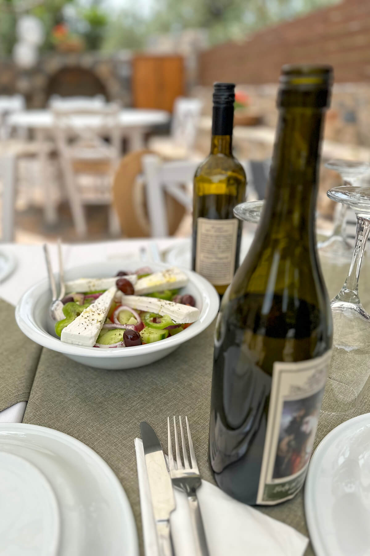 Bottles of wine set on a table with a Greek salad