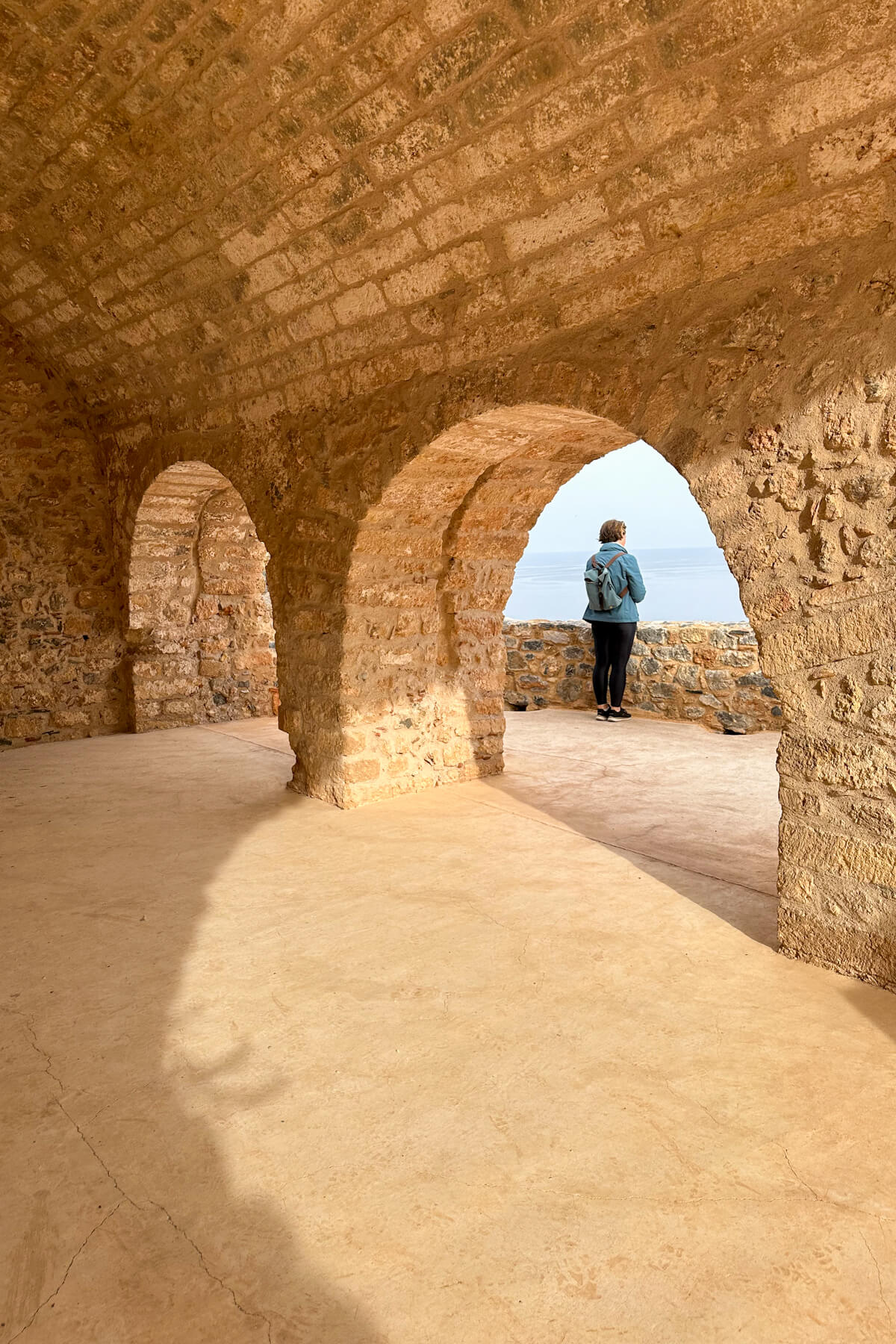 A woman looking out over the Mediterranean Sea under a stone archway
