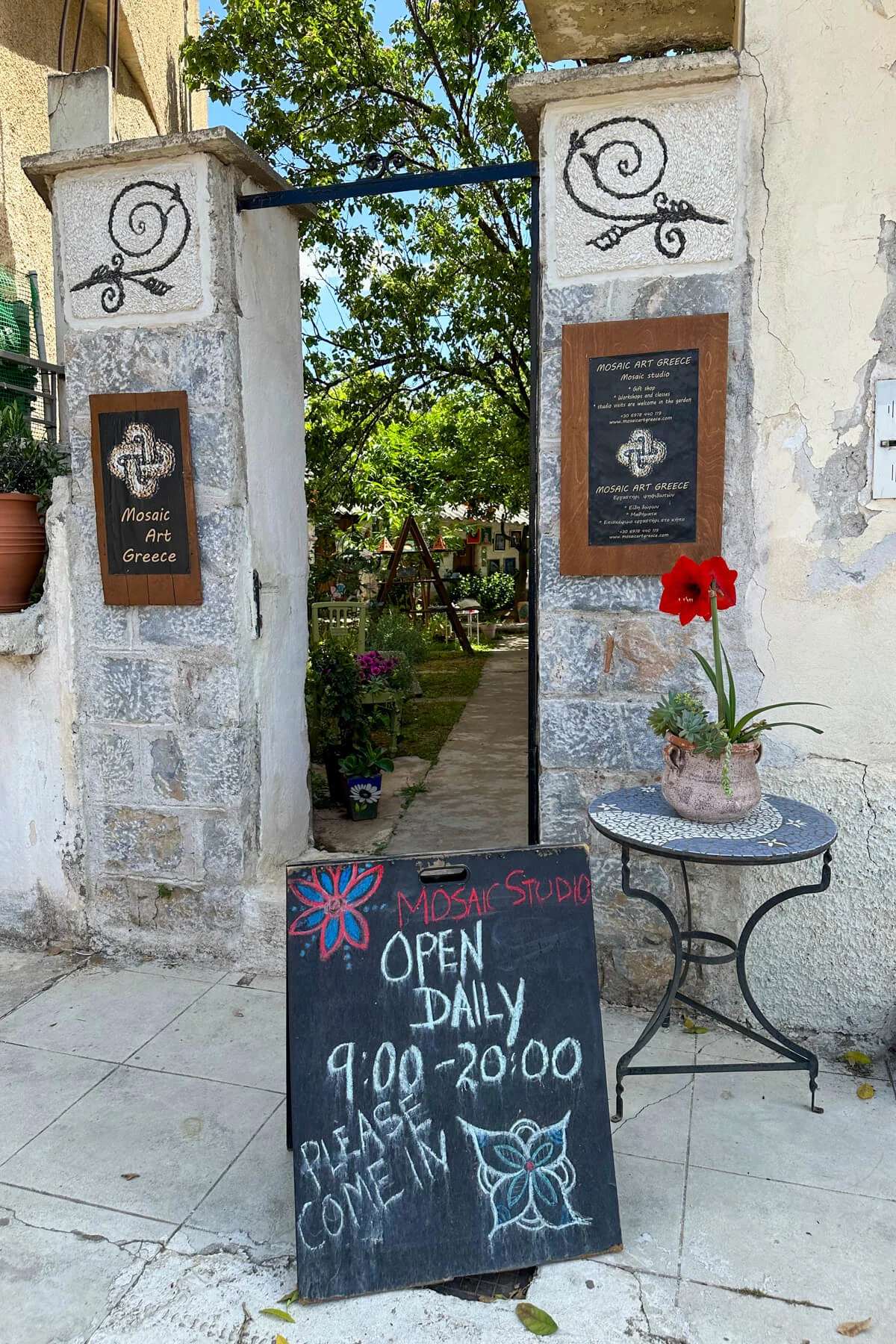 Entrance to the mosaics workshop with three signs, a small round table with a red potted flower sitting on it