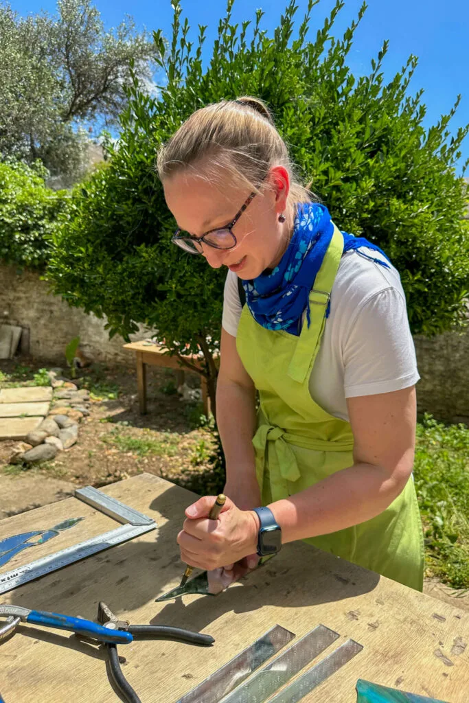 Lauren in a blue scarf and neon green apron working on one of the styles of mosaics