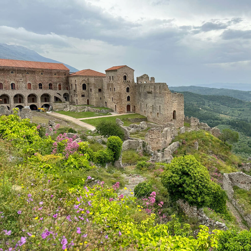 A view of the monastery at Mystras with greenery, flowers, and mountains