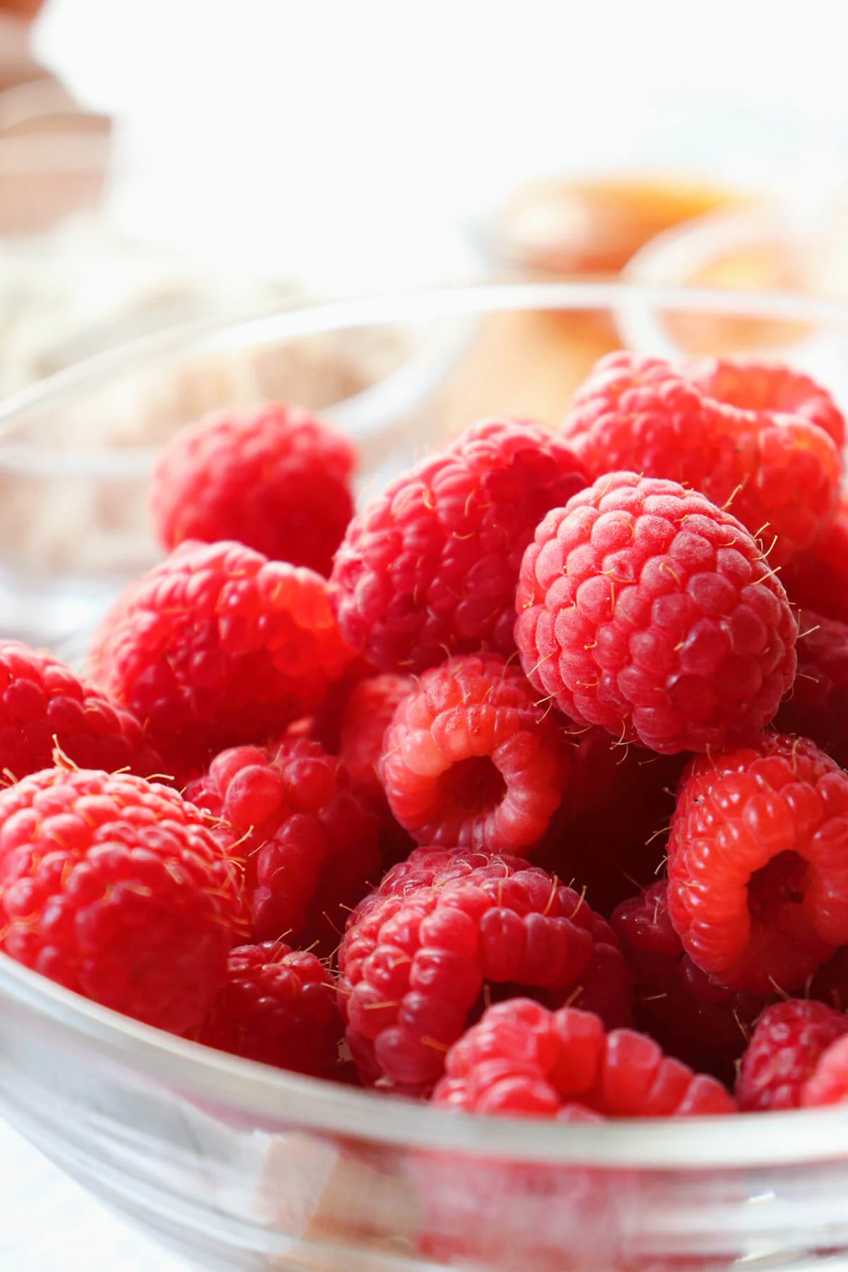 A glass bowl of raspberries with sunlight shining on them