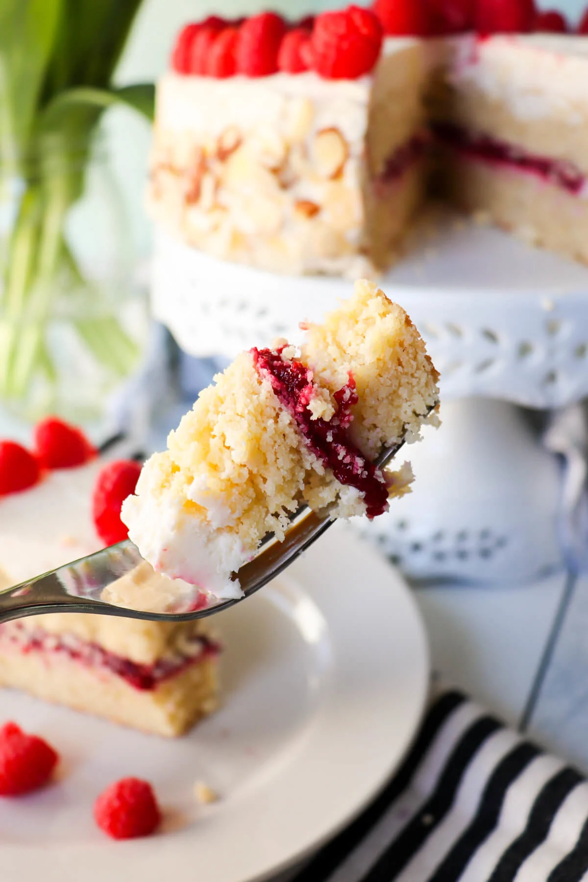 A fork with a bite of low carb almond raspberry cake in front of the entire cake