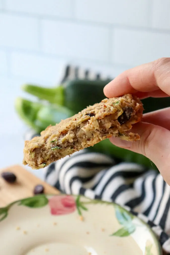A hand holding up a keto zucchini breakfast cookie with a bite out of it