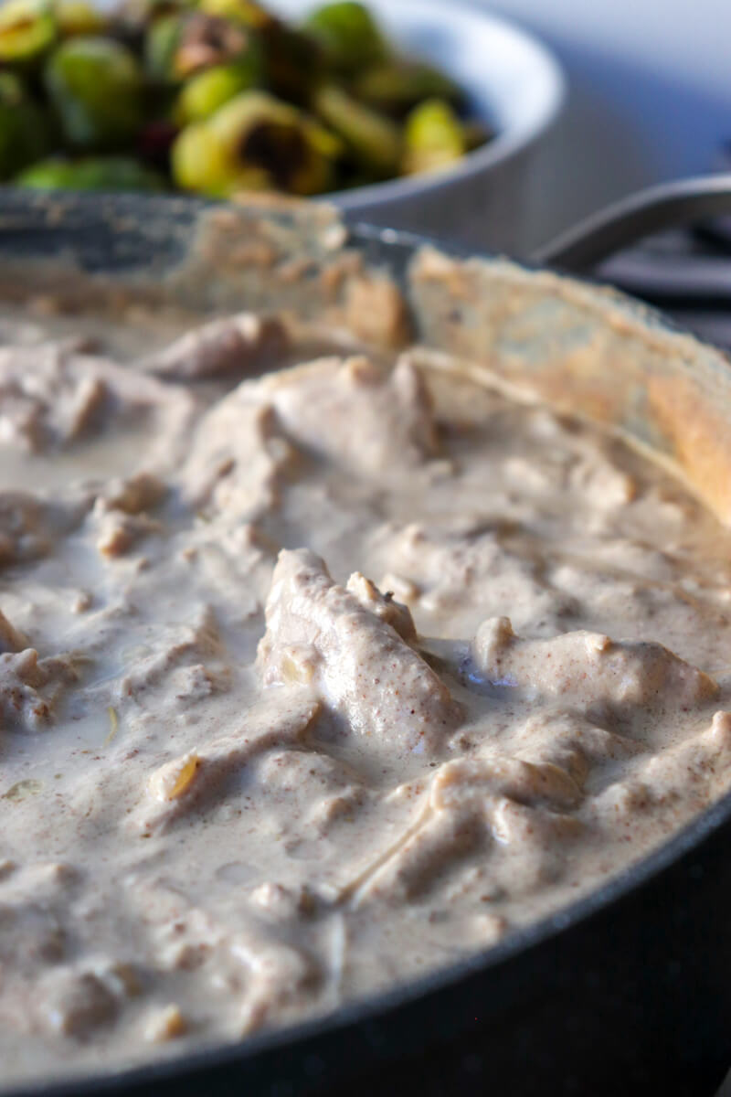 A closeup of the skillet of Georgian satsivi with a white dish of Brussels sprouts in the background.