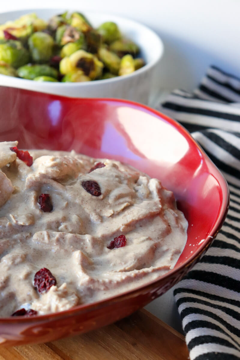 A closeup of a red bowl of Georgian satsivi with a white dish of Brussels sprouts in the background.