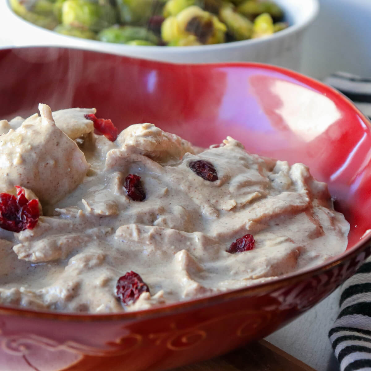 A large red serving bowl with Georgian satsivi and a dish of brussels sprouts in the background.