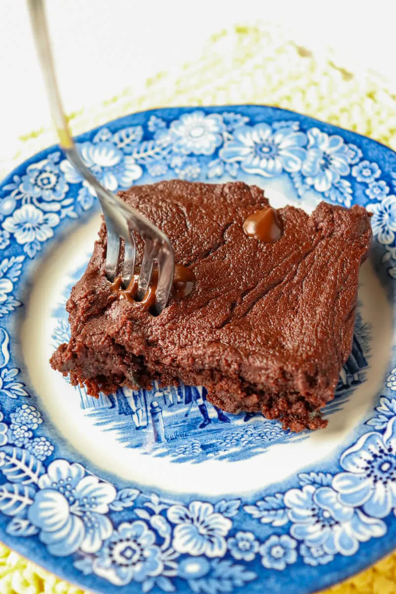 A keto zuccini brownie (low carb) on a blue and white plate with a fork in it.