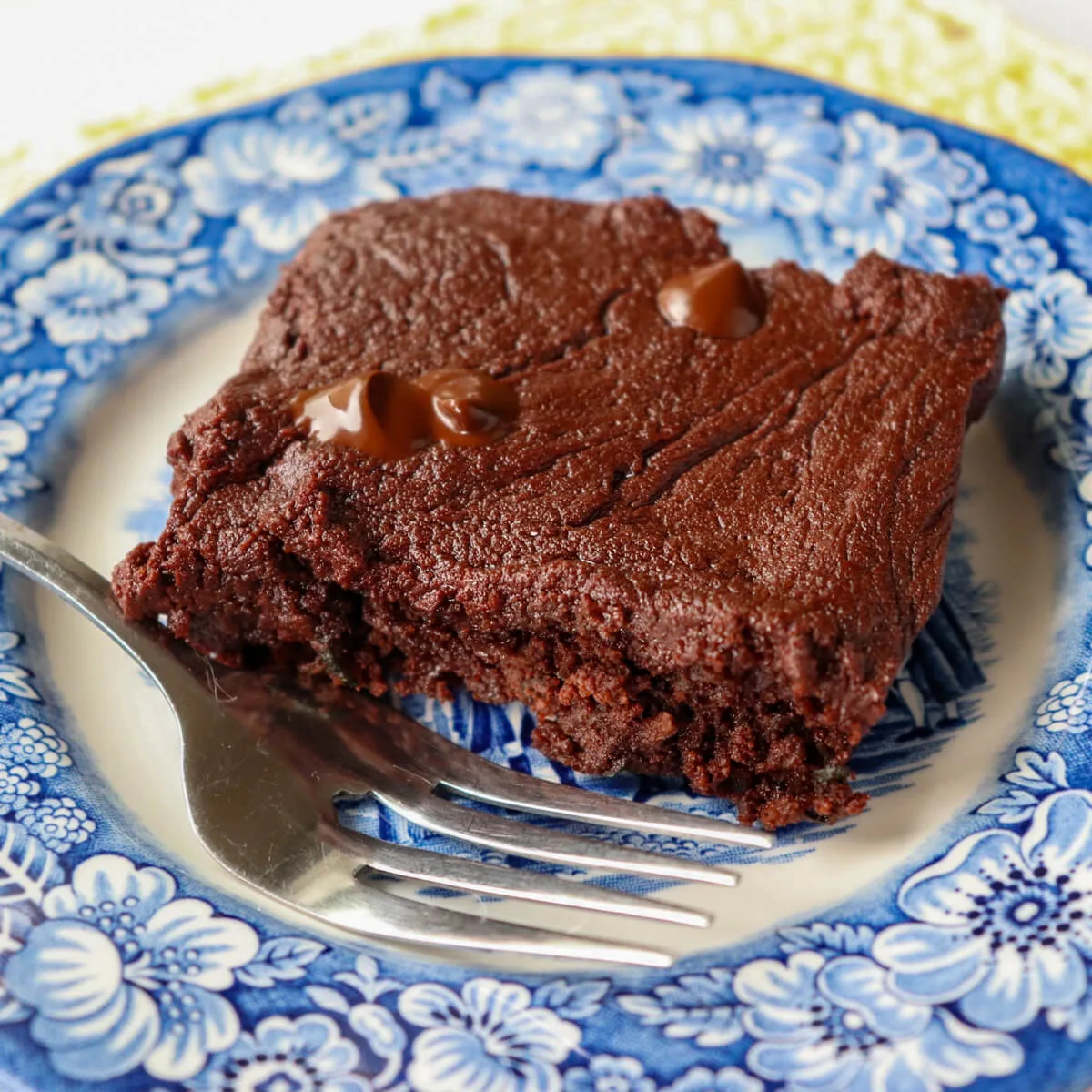 A keto zuccini brownie (low carb) on a blue and white plate with a fork next to it.