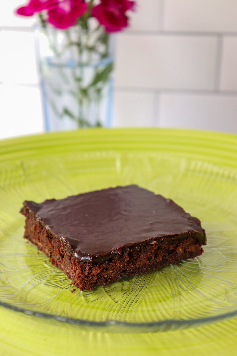 One keto zucchini brownie on a clear plate on top of a green plate.