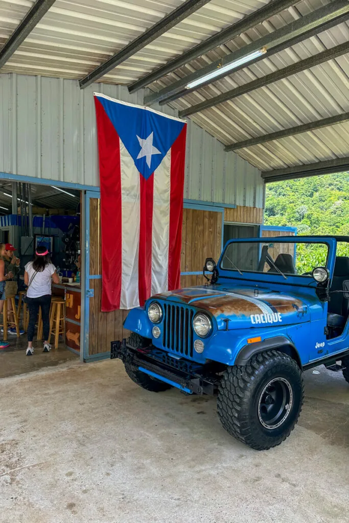 The front of a building with an overhang, a large Puerto Rican flag, and a bright blue Jeep