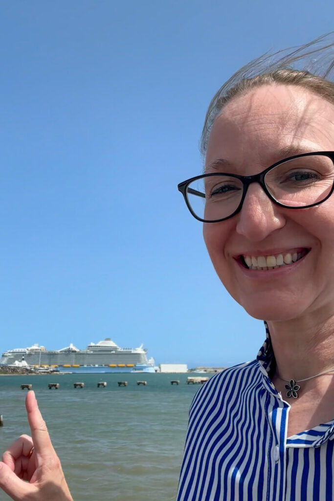 A woman in glasses pointing at a Royal Caribbean cruise ship in the background.