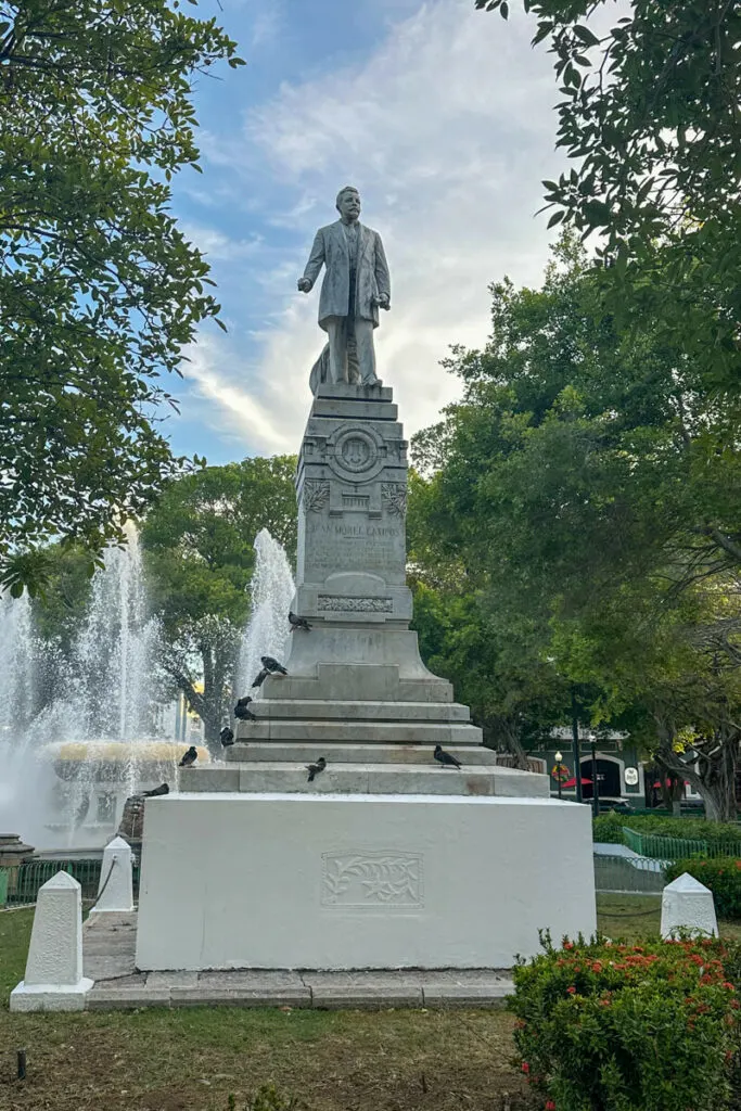 A statue of a man on a pedestal in front of the Lion Fountain in Ponce