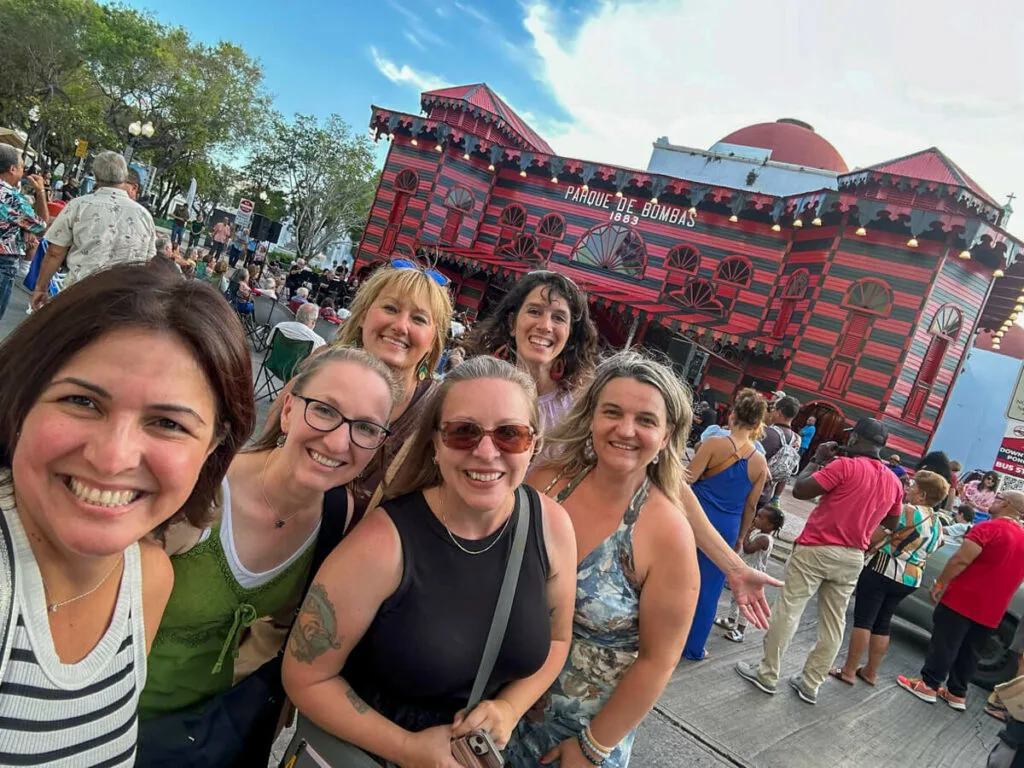 A group of women smiling at the camera in front of the striking black and red old Firehouse of Poncé