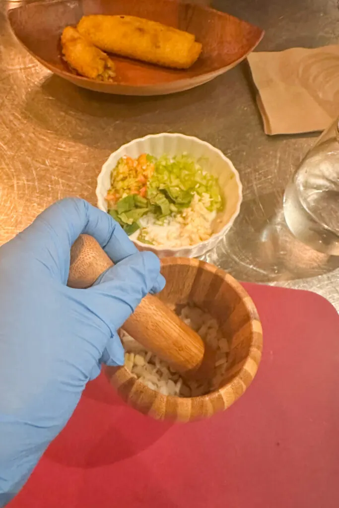 A blue gloved hand using the pestle and mortar to make sofrito