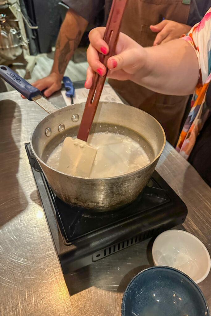 A hand stirring the coconut milk cooking over a pan