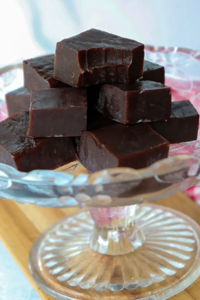 A glass plate of keto fudge with one piece on top with a bite taken out