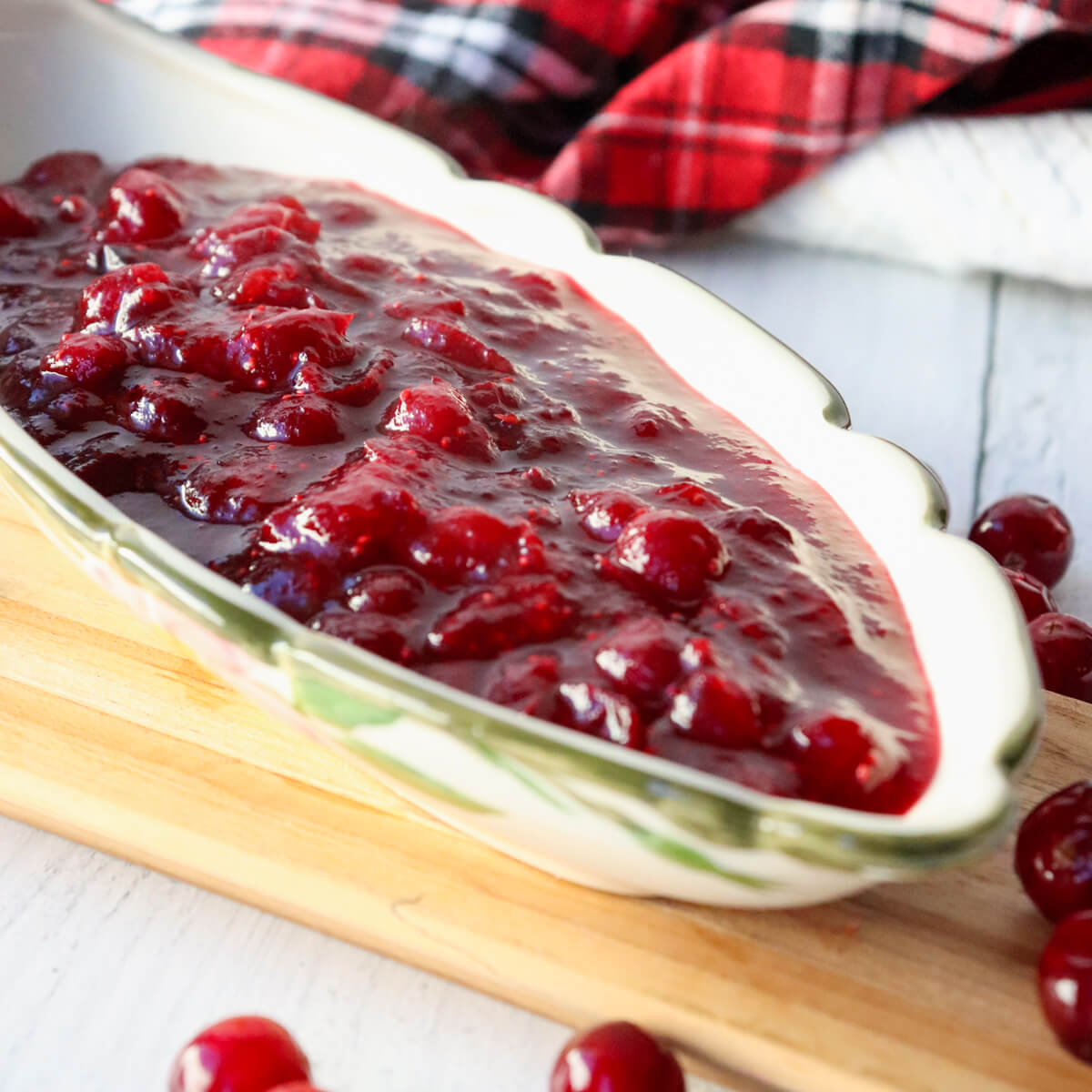 Boat style dish filled with homemade rich red cranberry sauce on a wooden platter with cranberries around.