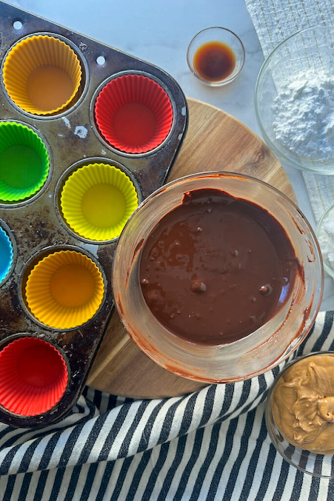 Overhead view of a muffin tin with silicone cups next to a bowl of chocolate