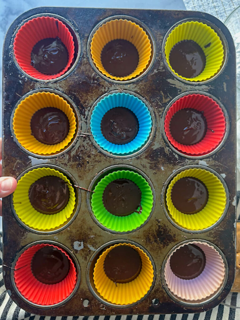 Overhead view of a muffin tin with silicone cups and a layer of chocolate