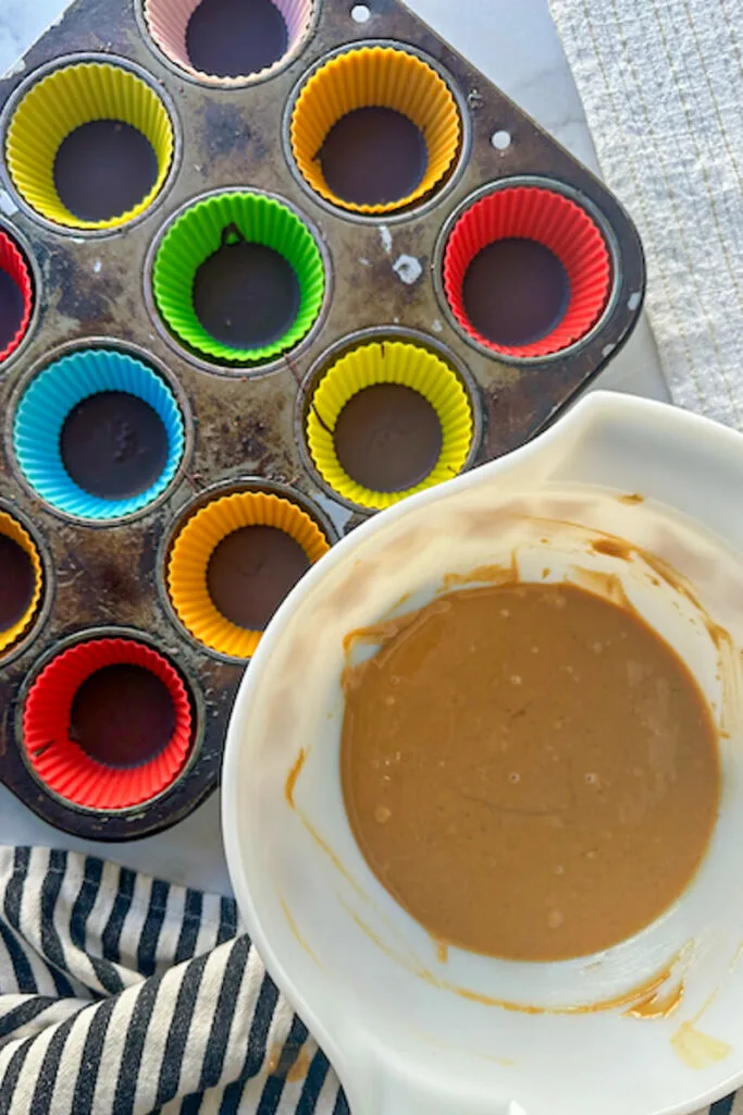 Overhead view of a bowl of peanut butter filling next to cups with chocolate a chocolate layer