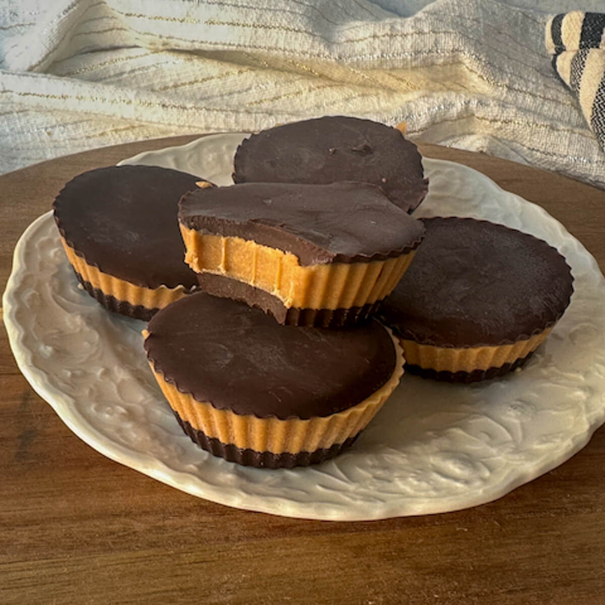 A white plate of keto peanut butter cups in a stack with the top one having a bite taken out.