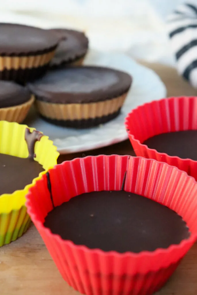 Low carb peanut butter cups in yellow and red silicone baking cups with a plate with a stack in the background