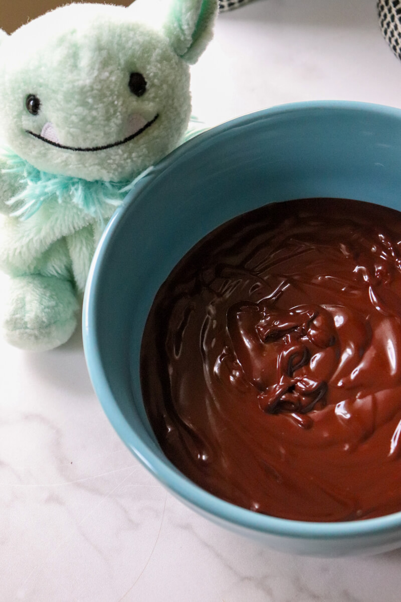 Overhead view of a blue bowl of keto chocolate ganache and a small stuffed green goblin behind it.