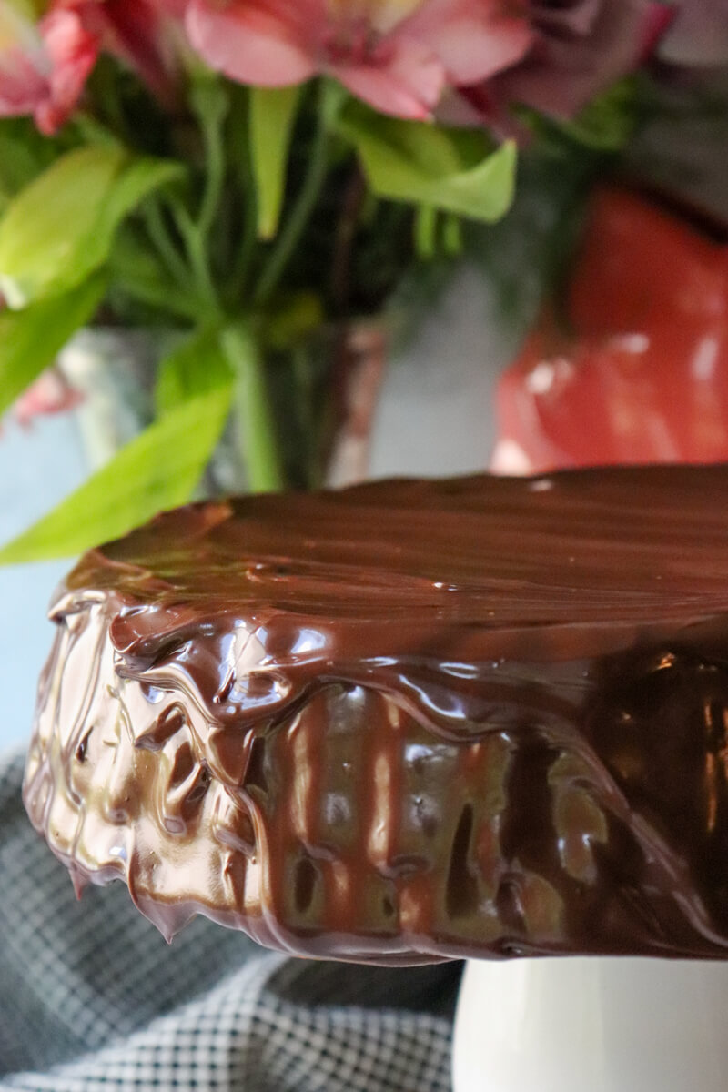 A low carb chocolate zucchini cake on a white pedestal with a keto chocolate ganache.