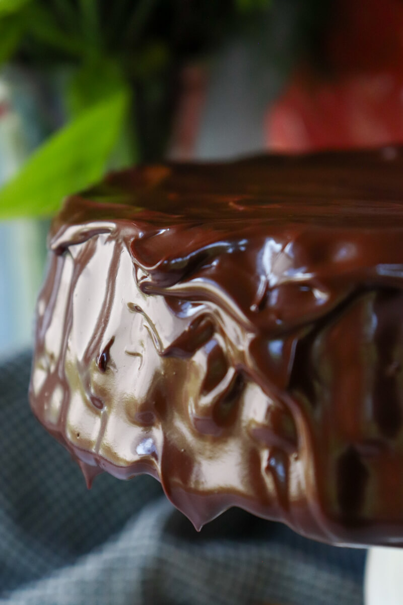 A closeup of a low carb chocolate zucchini cake on a white pedestal with a keto chocolate ganache.
