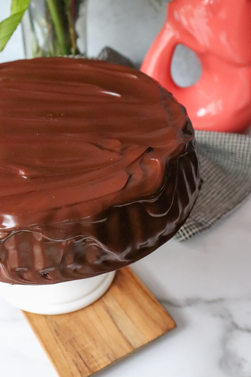 A low carb chocolate zucchini cake on a white pedestal with a keto chocolate ganache.
