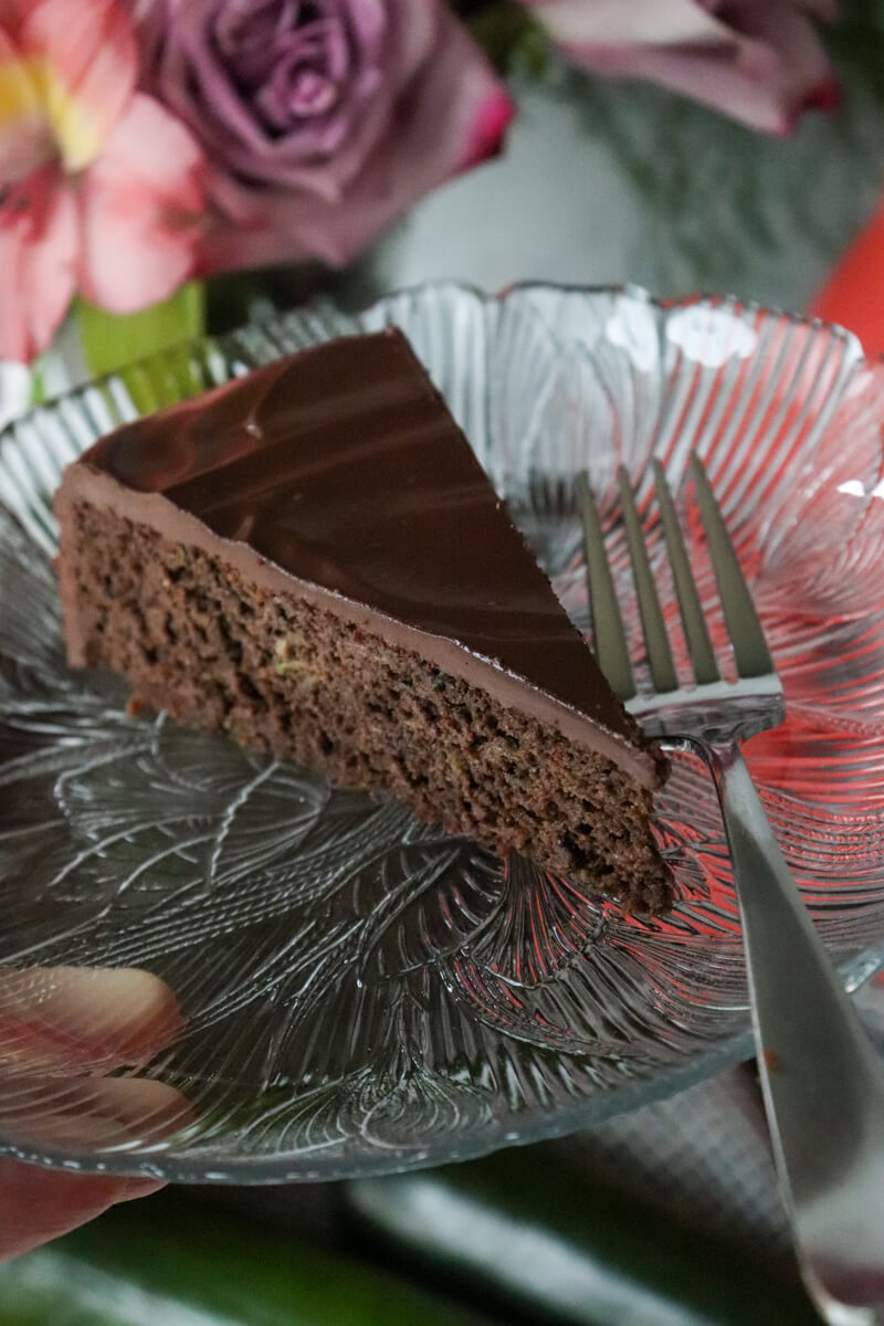A piece of keto chocolate zucchini cake on a decorative glass plate.