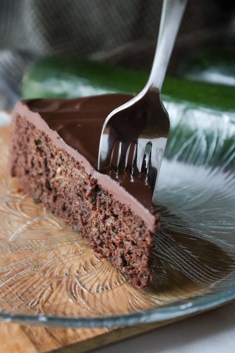 A fork about to take a bite out of a piece of keto chocolate zucchini cake on a decorative glass plate.