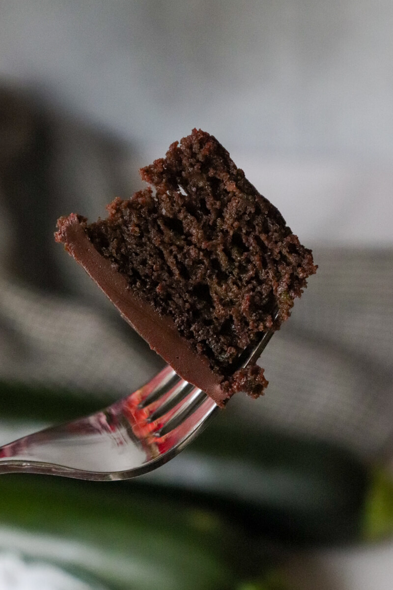A fork with a bite of keto chocolate zucchini cake on the tip. The rest of the cake is seen in the background.