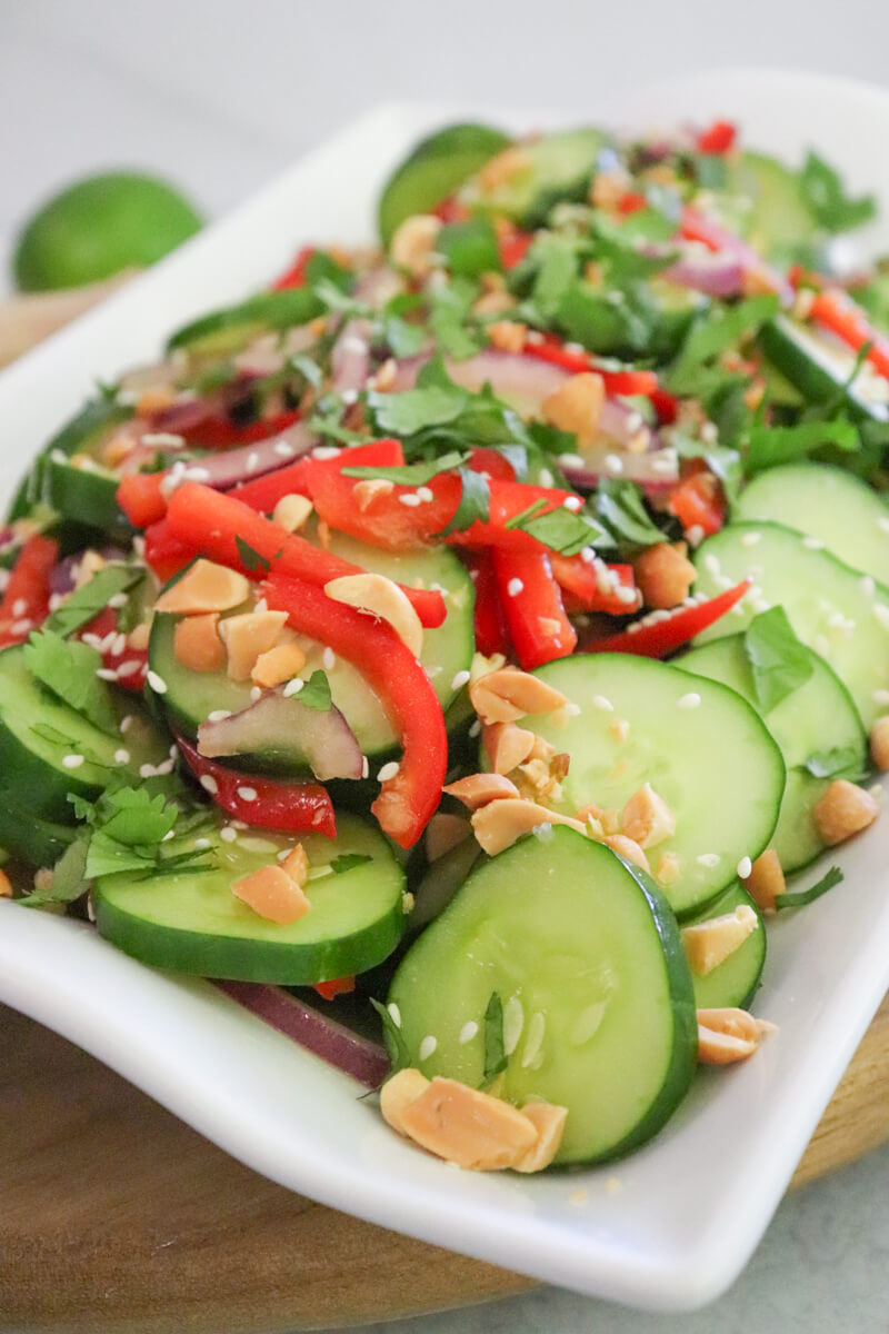 Front closeup view of a platter of Thai cucumber salad with cilantro, peanuts, and sesame seeds on top.