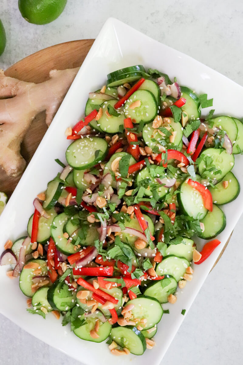 Overhead view of a platter of Thai cucumber salad with cilantro, peanuts, and sesame seeds on top.