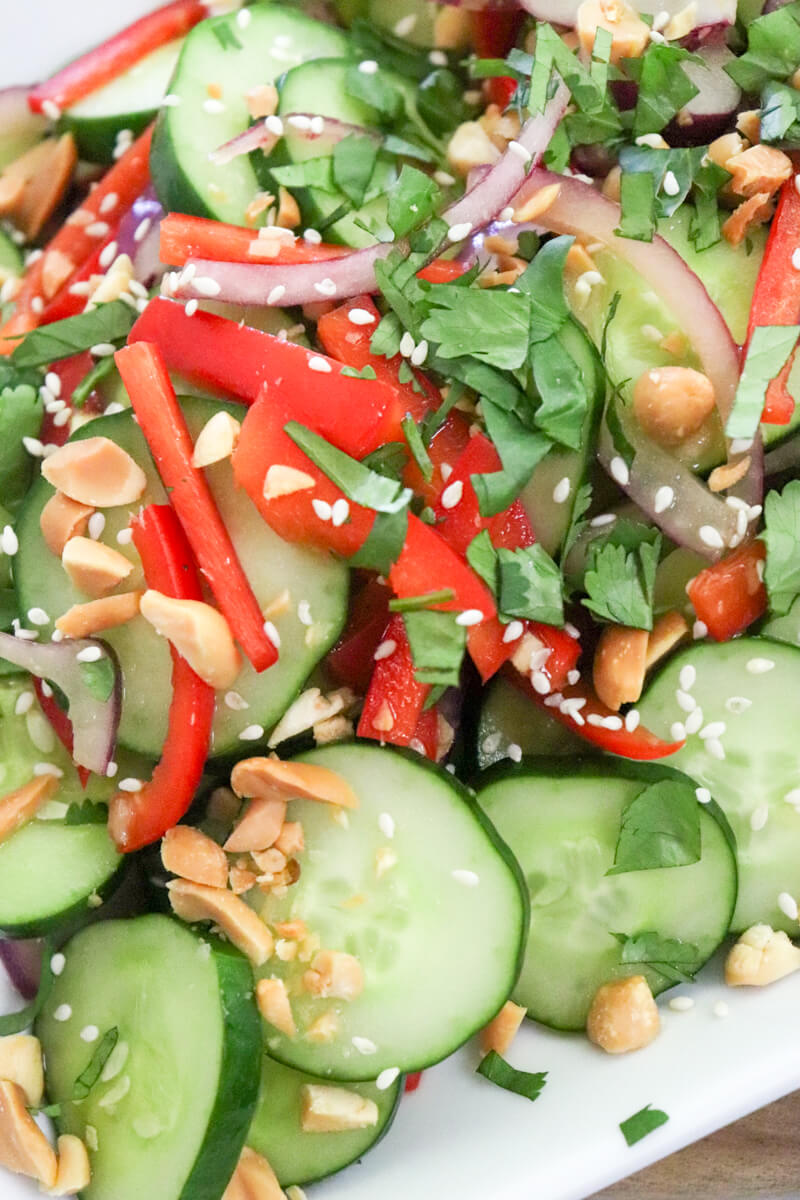 Overhead closeup view of a platter of Thai cucumber salad with cilantro, peanuts, and sesame seeds on top.