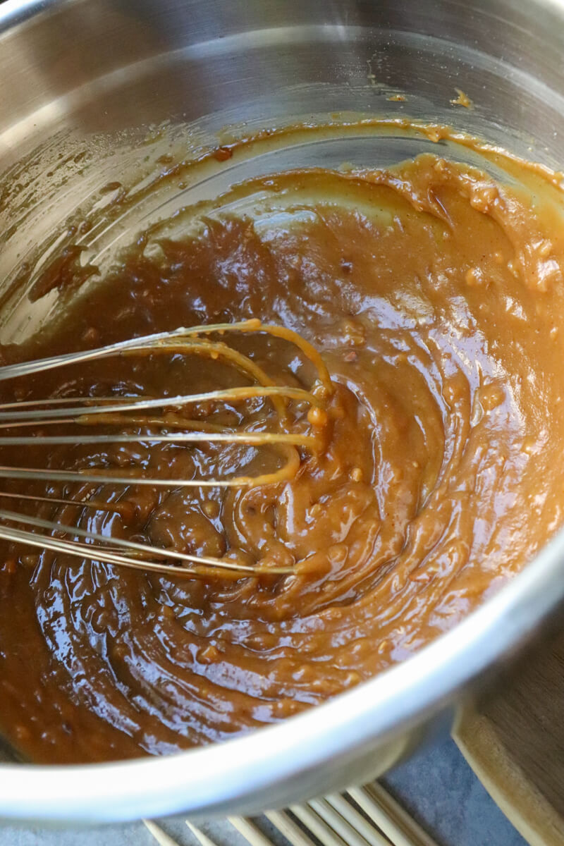 Overhead view of a metal bowl with a whisk stirring the keto peanut sauce