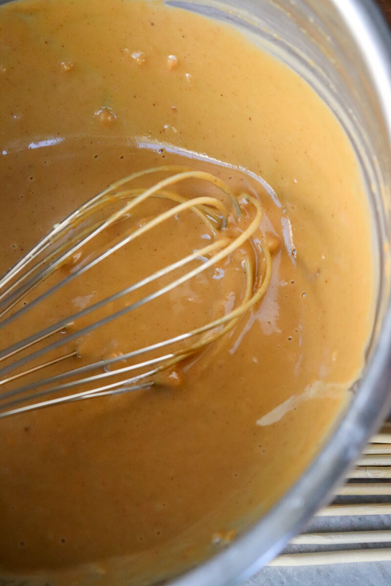 Overhead view of a metal bowl with a whisk stirring the keto peanut sauce