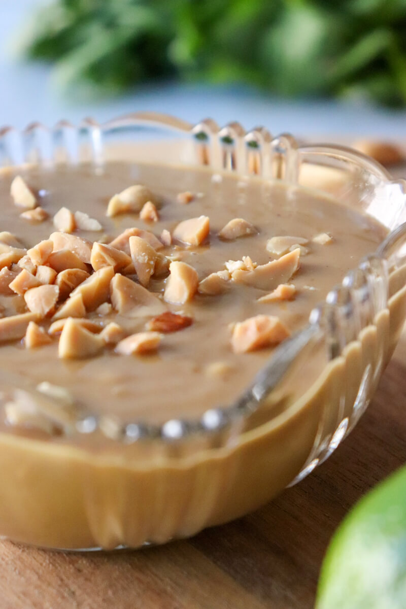 A close up of a glass bowl of low carb Thai peanut sauce sprinkled with extra peanuts