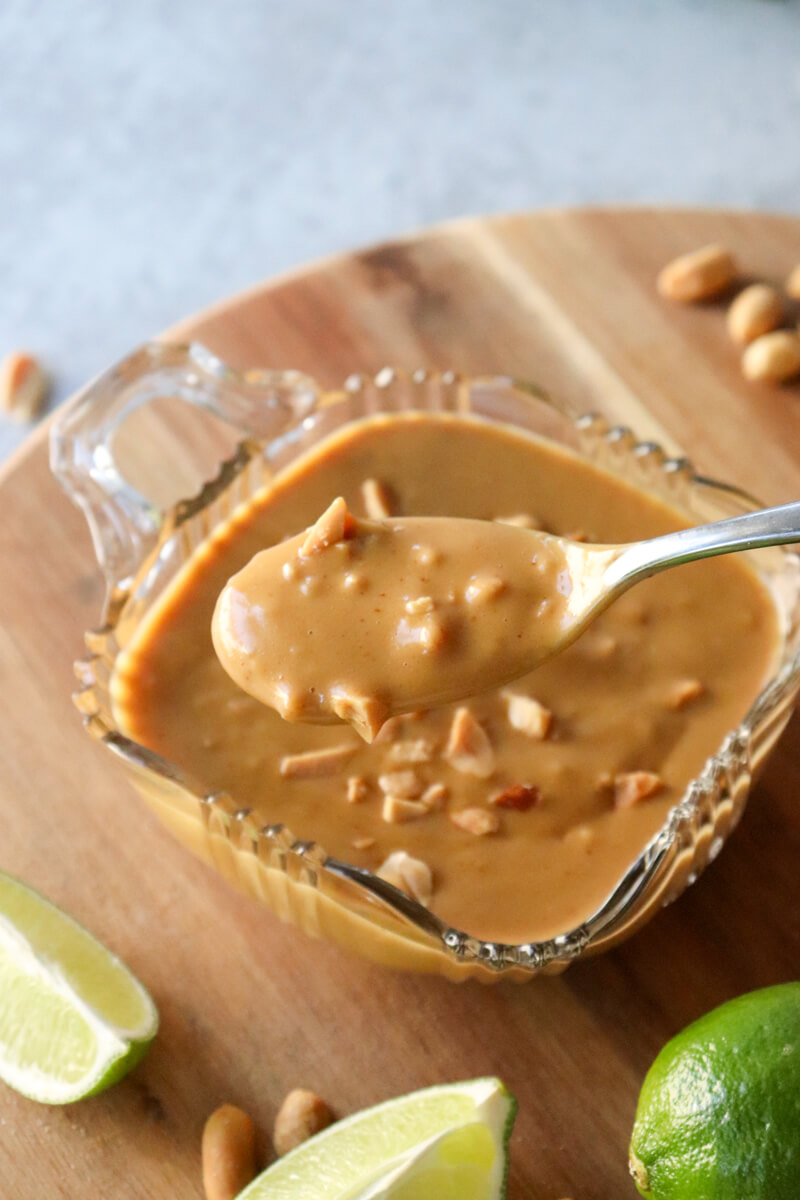 A close up of a glass bowl of low carb Thai peanut sauce sprinkled with extra peanuts, and a spoon lifting some out