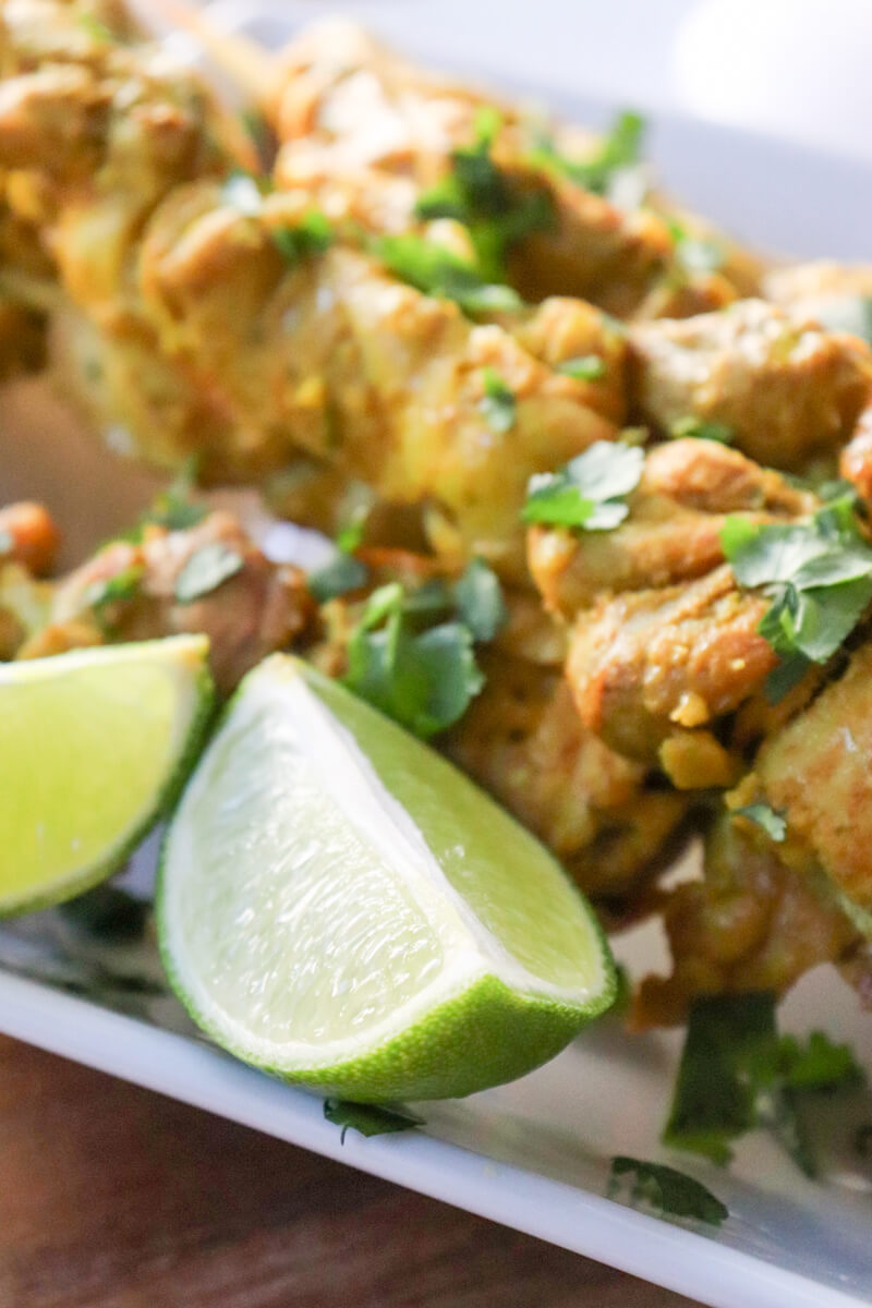 Keto chicken satay on skewers on a white serving dish with lime slices