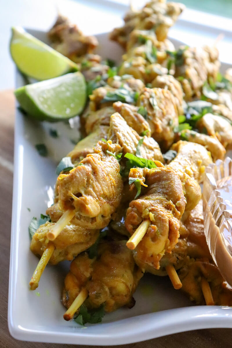 Keto chicken satay on skewers on a white serving dish with lime slices