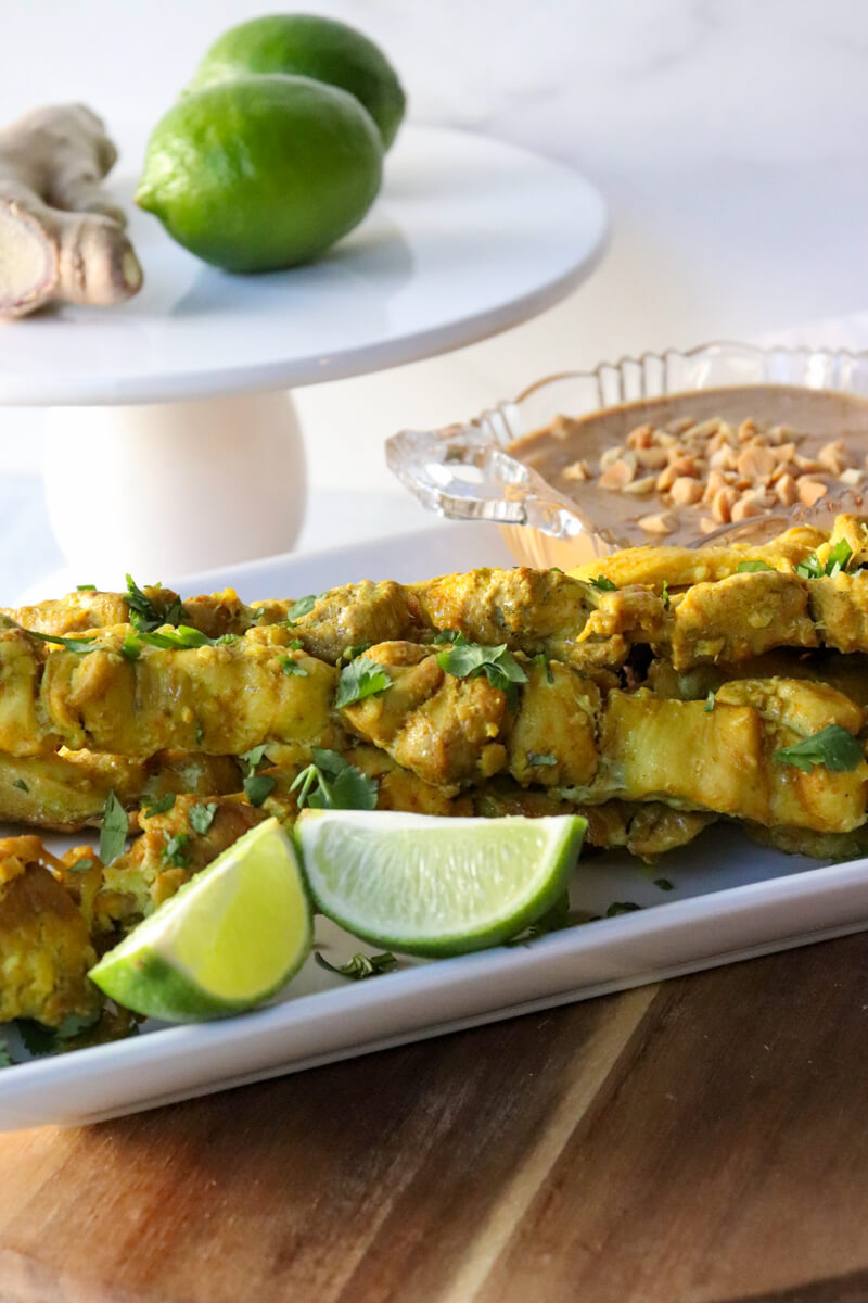 Keto chicken satay on skewers on a white serving dish with peanut sauce