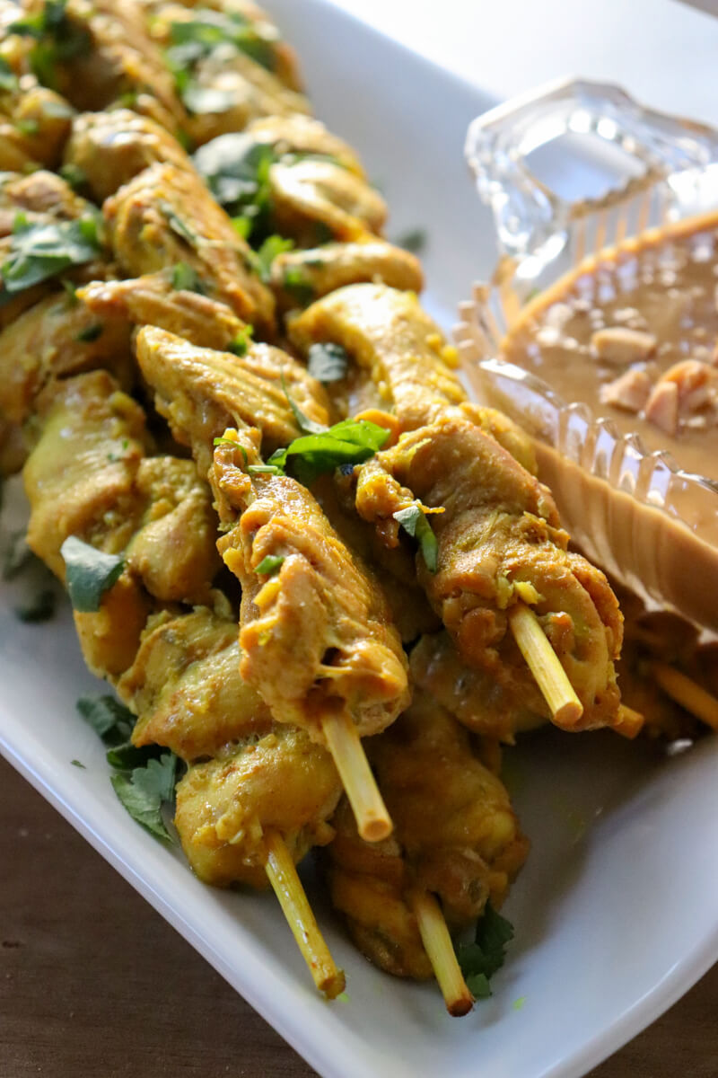 Keto chicken satay on skewers on a white serving dish with peanut sauce